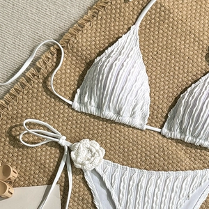 Detailed view of white crinkled bikini with handmade crochet flower ties on straw mat
