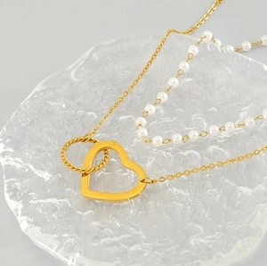 Gros plan d'un collier double chaîne dorée avec pendentif cœur et perles sur plateau