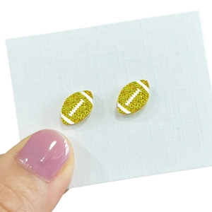 Detailed view of gold glitter rugby football stud earrings displayed on a white card