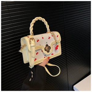 Detailed close-up of cherry print handbag with woven handle and gold floral lock
