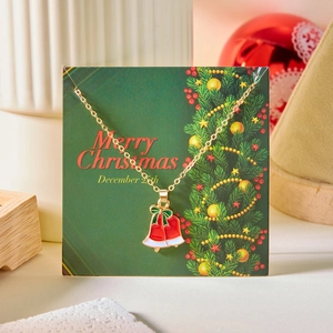 Detailed view of a gold Christmas bell necklace with a red enamel finish on a gift card