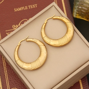 Macro view of gold hoop earrings featuring intricate cross-grid embossed texture detail