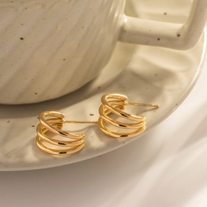 Polished 18K gold triple line stainless steel hoop earrings on a ceramic dish