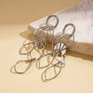 Close-up of silver geometric layered teardrop earrings resting on a white stone base