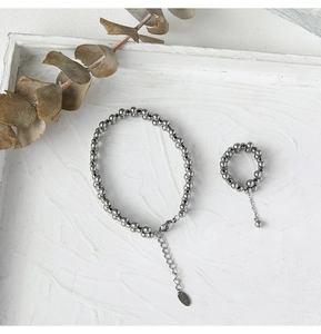 Macro shot of silver beaded bracelet and ring set on white tray with eucalyptus leaves