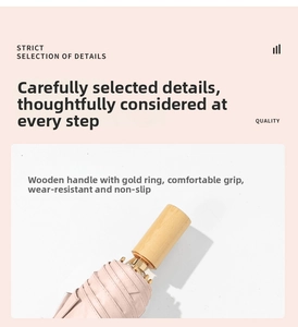 Detail of a light pink folding umbrella with a premium wooden handle and gold metal ring