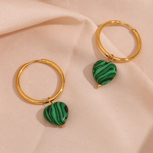 Detailed view of heart-shaped malachite pendants on gold hoops over pink satin fabric