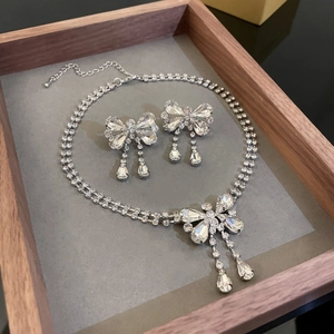 Detailed view of silver bow-knot crystal necklace and earrings set on a grey tray