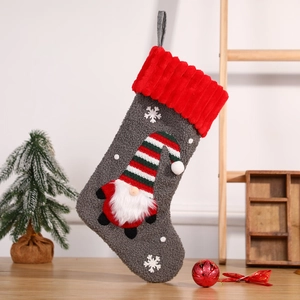 Gray plush Christmas stocking with gnome embroidery and red ribbed cuff hanging on wood