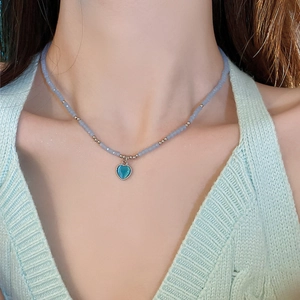 Close-up of a blue beaded heart necklace on a model with a soft green knit top