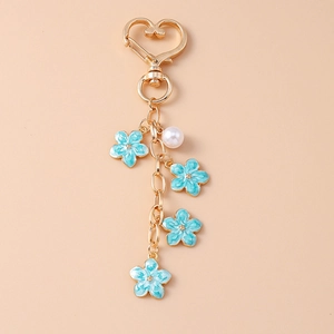 Detail of a gold keychain featuring blue enamel flowers and a white pearl bead decoration
