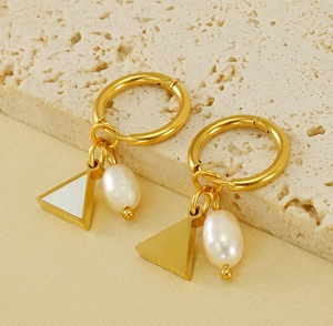 Detail of 18K gold earrings with white triangle charm and natural pearl on stone surface