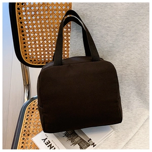 Detail of minimalist black canvas lunch bag placed on a rattan chair for daily use