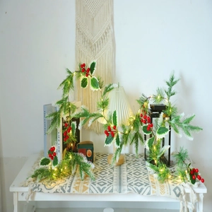 Detailed view of artificial pine garland with red berries and warm LED lights on a white table