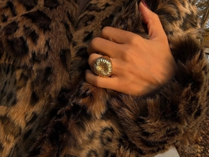 Golden textured statement ring shown on hand with a stylish leopard print coat background