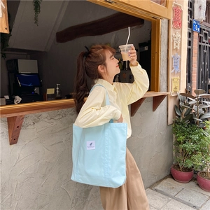 Close-up of a light blue canvas tote bag with front decorative label on model shoulder