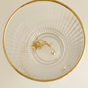 Close-up of golden heart pendant necklace placed inside a ribbed glass on beige background
