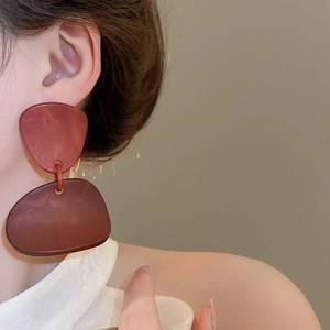 Detailed close-up of dark reddish-brown acrylic geometric earrings on model ear