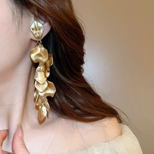 Close-up of elegant gold long tassel earrings with metallic petals on a model