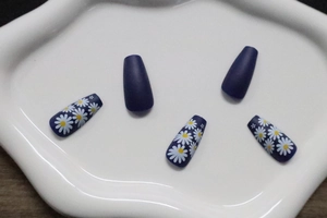 Detailed view of matte dark blue and white daisy floral press-on nail tips on white ceramic tray