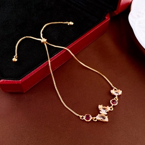 Bracelet papillon doré ajustable avec pierres roses à côté d'un écrin à bijoux rouge luxe