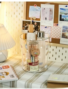 Clear cylindrical desktop trash can with cute cartoon bear stickers in a room setup