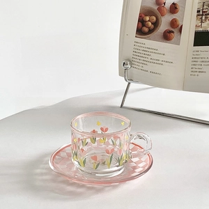 Detailed macro view of a floral glass mug and pink checkered saucer on a desk