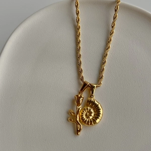 Gros plan d'un collier plaqué or 18 carats avec pendentifs rose et coquillage sur chaîne torsadée