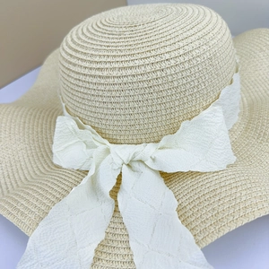 Close-up of hand-woven summer straw hat featuring an elegant white wavy lace bow