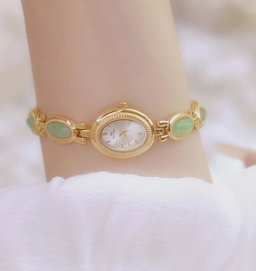 Detail view of gold-tone watch with green oval gemstone bracelet and white minimalist dial