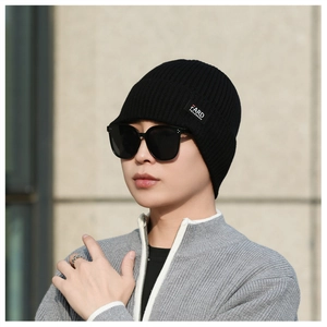 Detail of black knitted beanie featuring vertical ribs and a square fabric label on the side