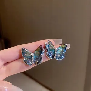 Boucles d'oreilles papillon dégradé bleu avec perles et cristaux tenues à la main