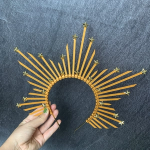Detail of gold sunburst halo crown with stars held against a dark textured stone background