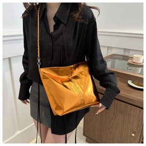 Close-up of metallic orange gold crossbody bag with chain strap worn by a model