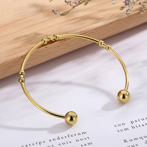 Macro detail of golden open heart bangle with bead accents on natural wood background