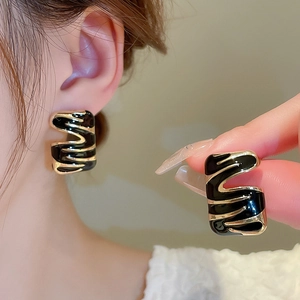 Close-up of black and gold wavy enamel earrings showing fine texture and modern style