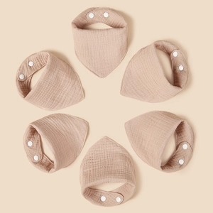 Detailed overhead shot of 6-pack beige cotton muslin baby bibs with snap buttons