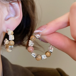 Détail de boucles d'oreilles créoles avec perles en œil de tigre et accents argentés