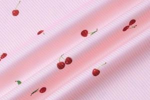 Détail macro du tissu en maille côtelée rose avec motifs de cerises rouges et feuilles