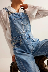 Detail view of light blue washed denim overalls with metal buckles and large front pocket
