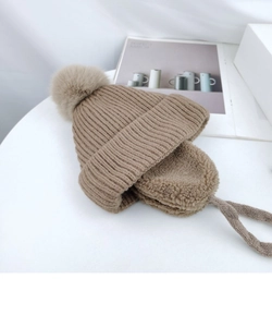 Close-up of brown knit ear-flapped hat with a fluffy faux fur pom and braided chin straps