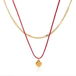 Détail d'un collier double couche avec chaîne dorée, cordon rouge et pendentif cœur