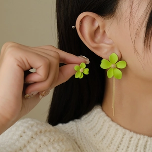 Detail shot of model wearing asymmetric green flower earrings with long tassels