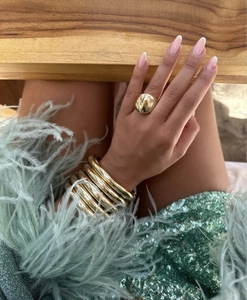 Close-up of polished gold wide dome ring and multi-layered bangles worn with luxury outfit