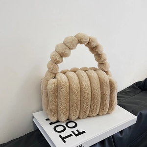 Chic beige plush handbag with quilted texture and beaded handle on a fashion book