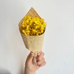 Close-up of mini yellow dried flowers bouquet in vintage newspaper wrap with jute twine