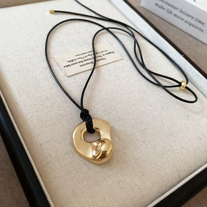Detail of a liquid metal texture gold pendant necklace on a beige fabric background