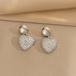 Elegant silver heart earrings with sparkling cubic zirconia on a warm textured surface