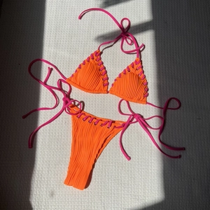 Orange ribbed bikini set with pink criss-cross side ties on a sunny white background
