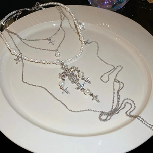 Macro detail of silver layered cross necklace with faux pearls on white ceramic tray